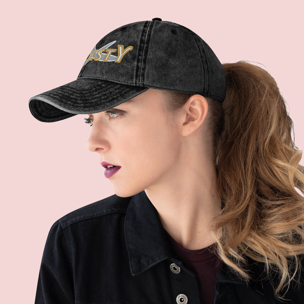 Side view of female wearing a black cap with 'MODESTY' text on a pink background