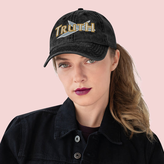 Person wearing a black cap with 'TRUTH' and a sword emblem on a pink background